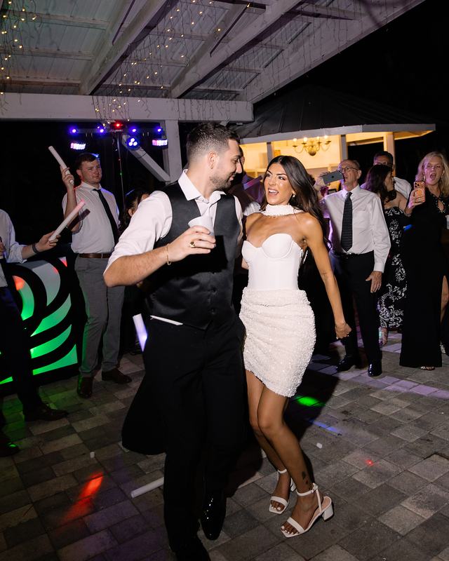 A bride and groom dancing in the middle of a packed dance floor under the DJ lights, guests dancing around them