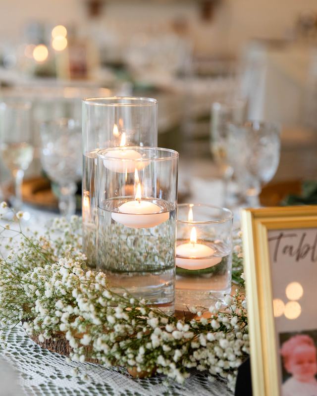 A table centerpiece of floating candles in glass cylinders ringed with baby’s breath, the table number in a gold frame beside it