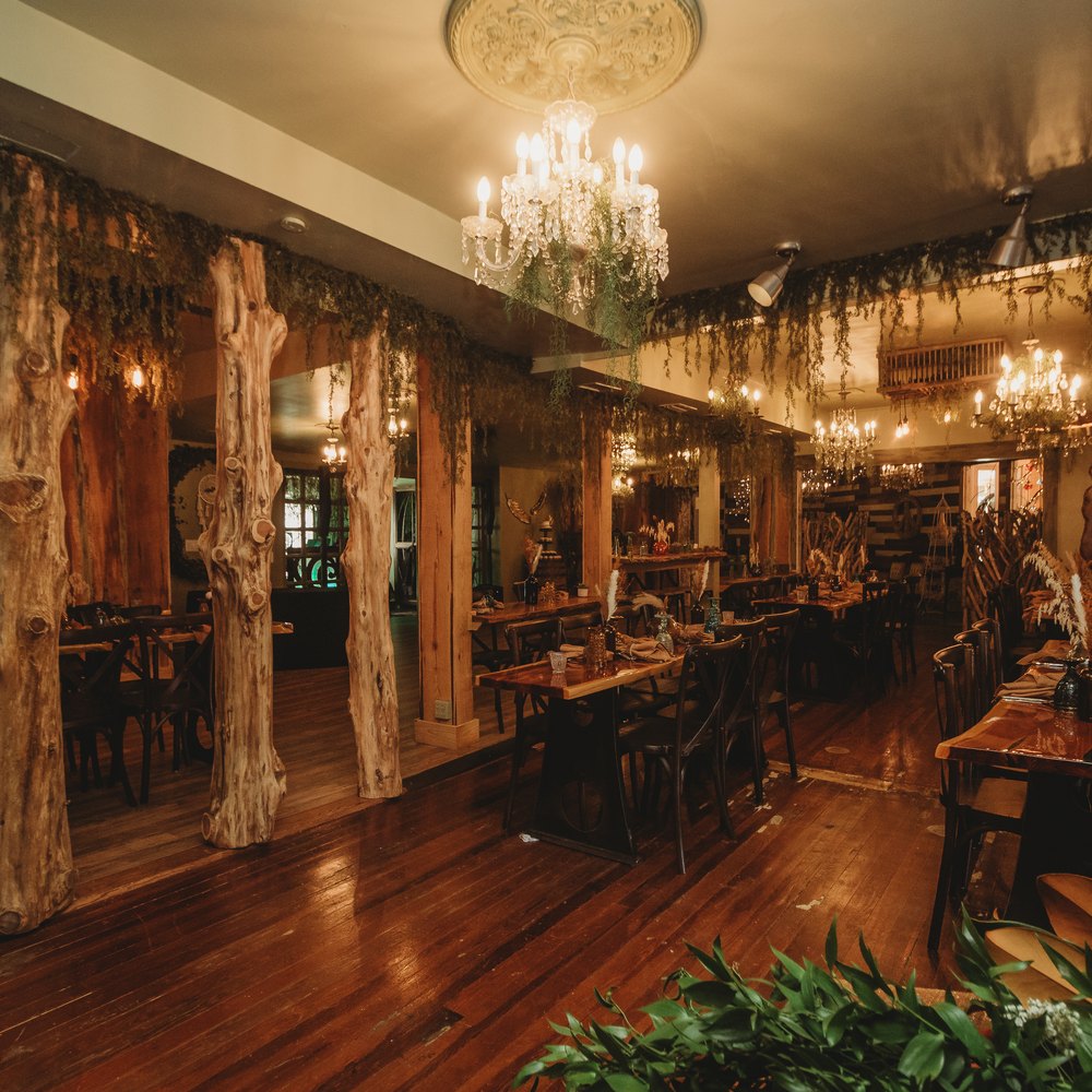 The BoHo dining room under crystal chandeliers, with carved wood columns and a polished plank floor