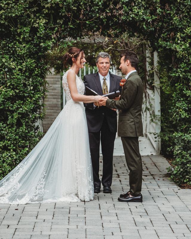 The officiant leading the vows as the couple hold hands beneath an ivy-covered arbor
