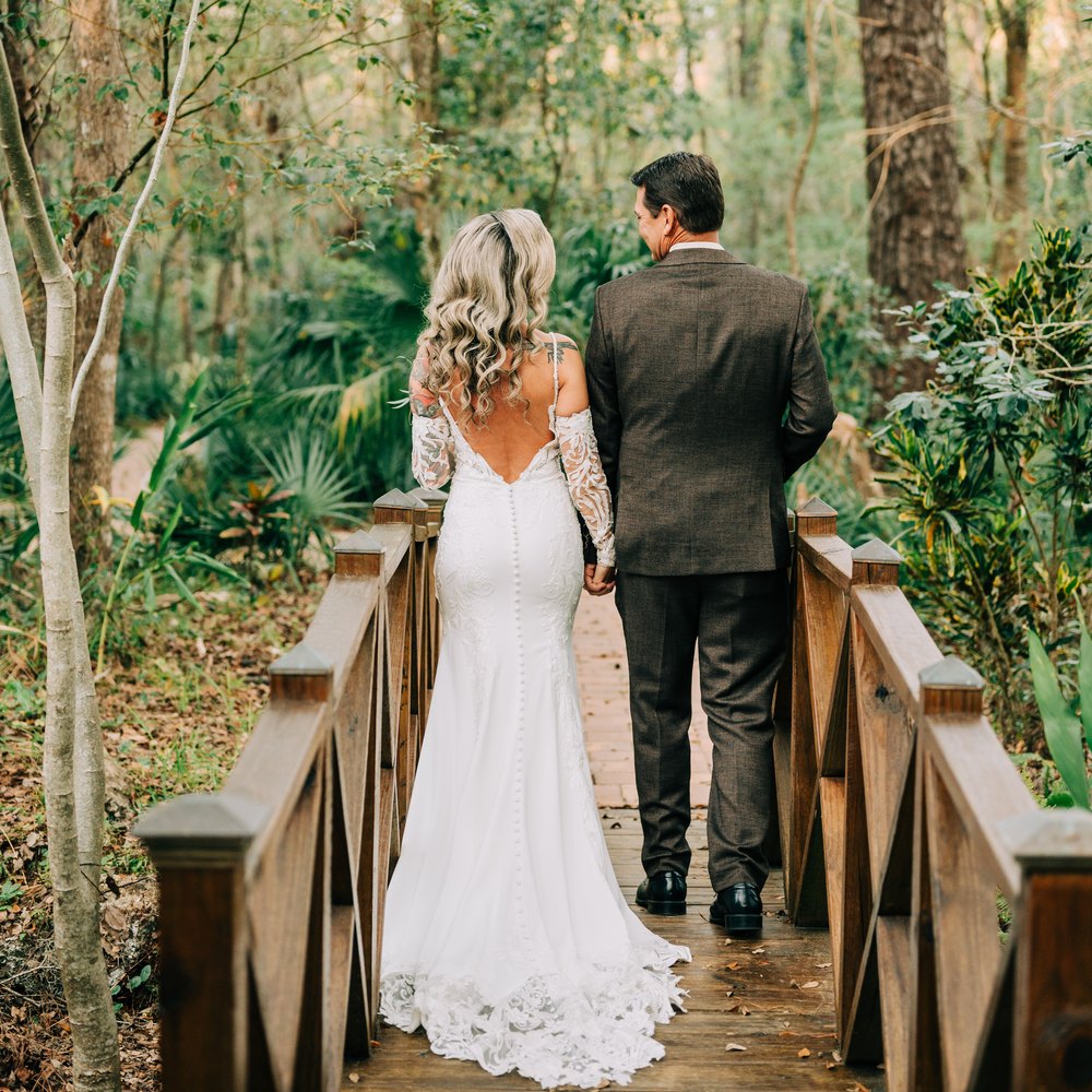 Bride and groom walking hand in hand across the wooden footbridge on the wooded path