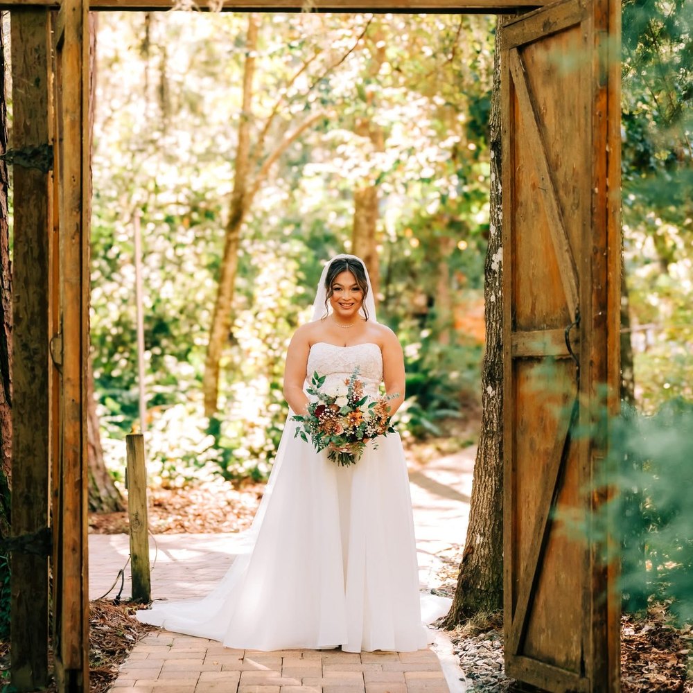 Bride with her bouquet framed by the open wooden doors on the wooded path
