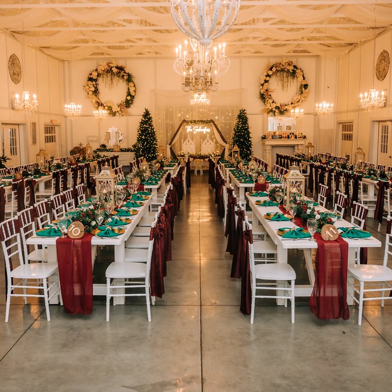 The Barn dressed for a winter wedding: long white tables with burgundy runners and emerald napkins, Christmas trees either side of the head table