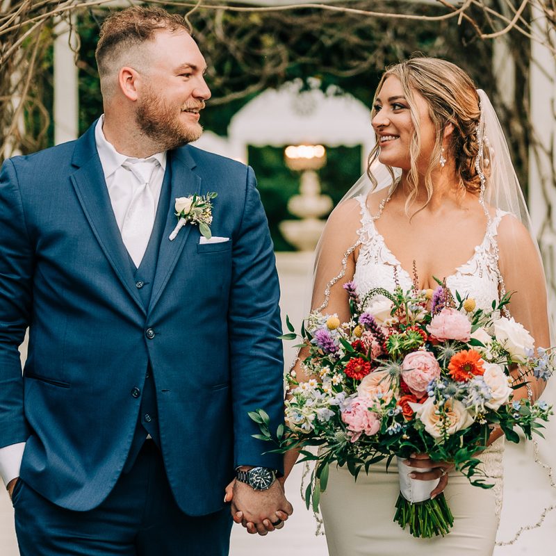 Bride and groom holding hands, the bride carrying a pink and coral garden bouquet