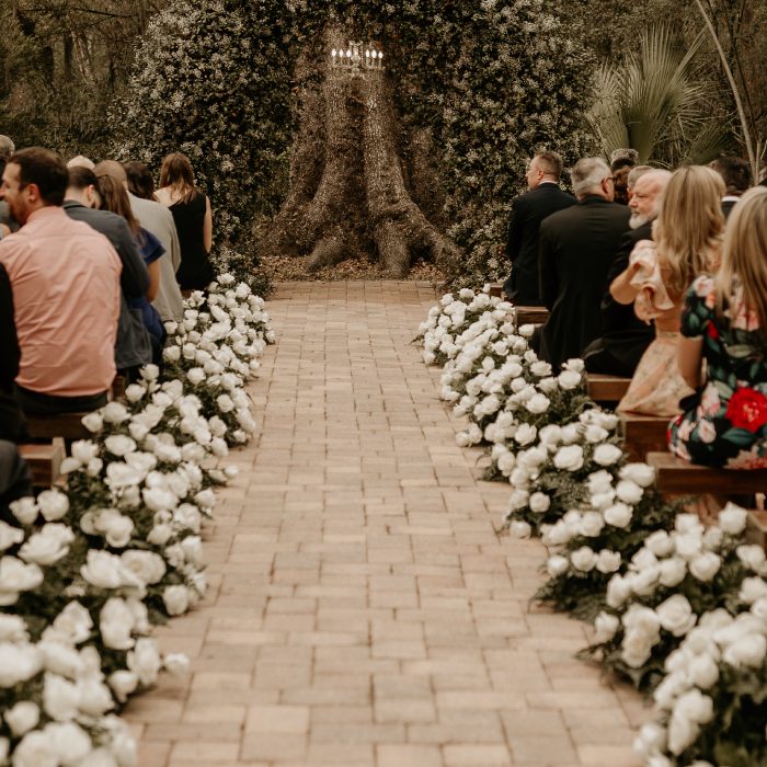 Ceremony aisle on a brick path lined with mounds of white flowers, guests seated either side