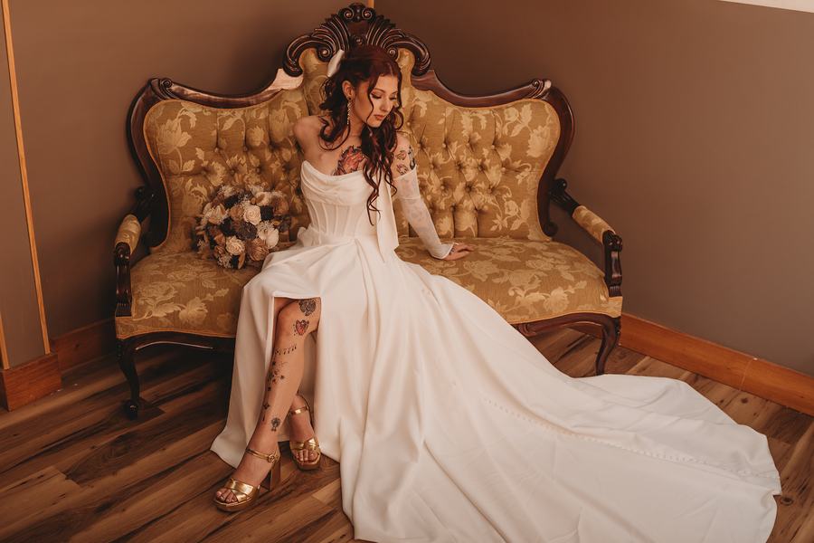 Bride in a long-sleeved gown sitting on a gold tufted Victorian settee, her bouquet beside her