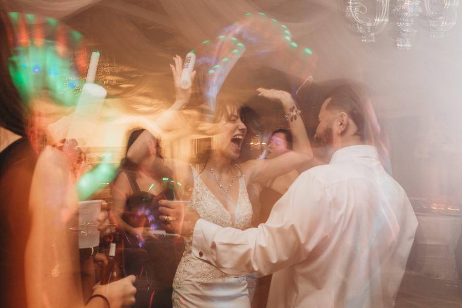Guests dancing with the bride and groom under colored light, arms in the air, the room a blur of motion