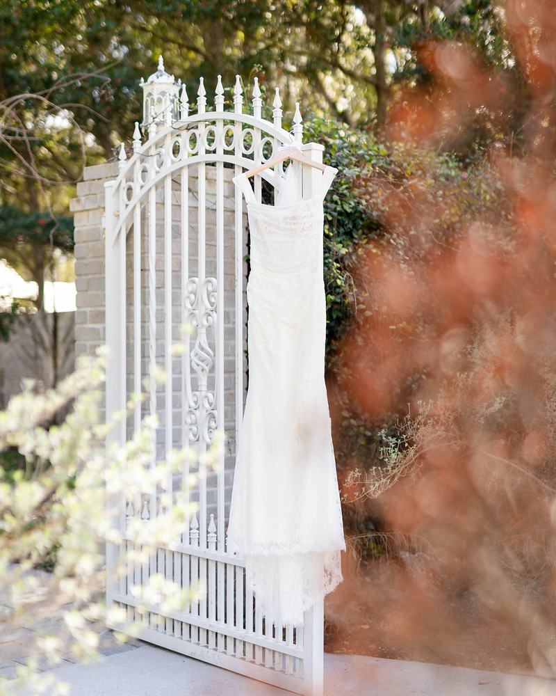 A wedding gown hanging from an open white wrought-iron garden gate