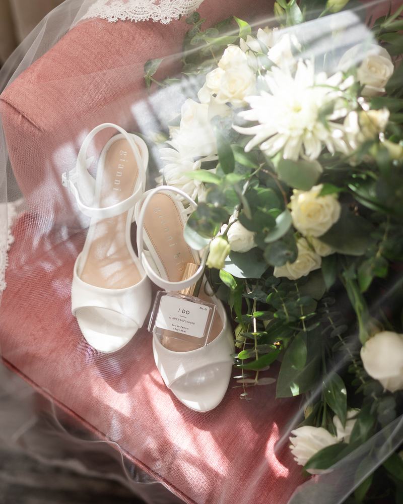 The bride's white strappy heels and a bouquet of white blooms laid on a pink cloth