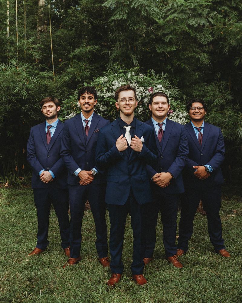 Groom and his groomsmen in navy suits standing on the lawn in front of the trees