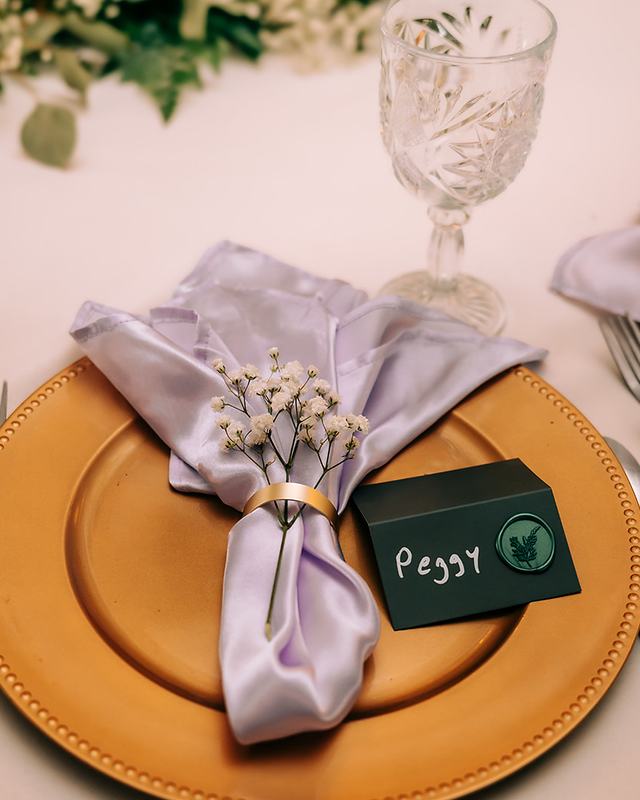 A place setting with a gold charger, a lavender napkin tied with baby’s breath and a handwritten name card